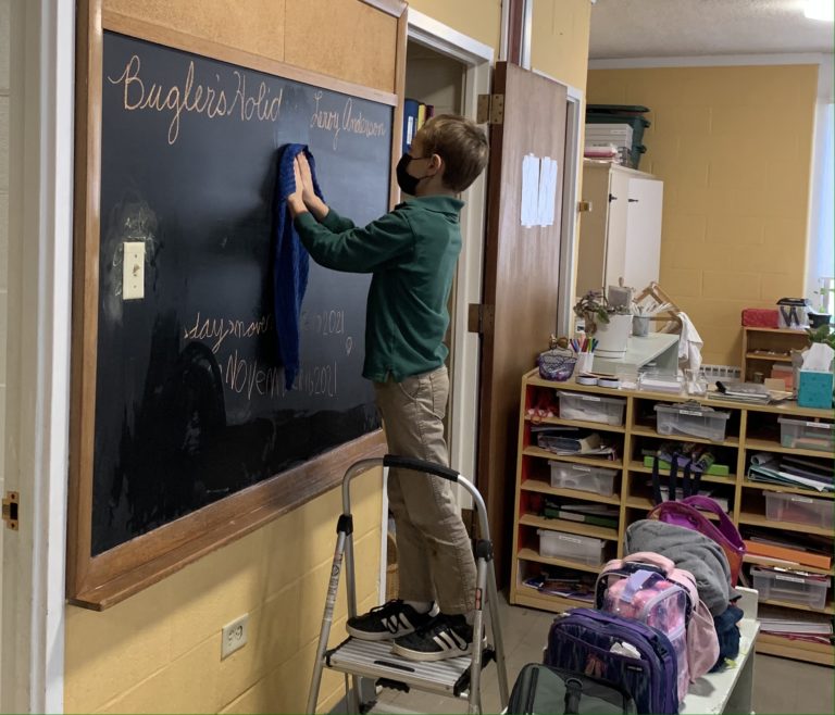 Student cleaning chalkboard in classroom